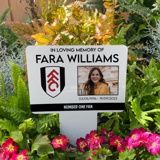 White Fulham football club memorial stake inserted in flower bed surrounded by colourful flowers in the garden