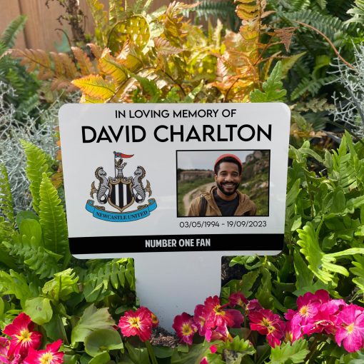 White Newcastle United football club memorial stake inserted in flower bed surrounded by colourful flowers in the garden