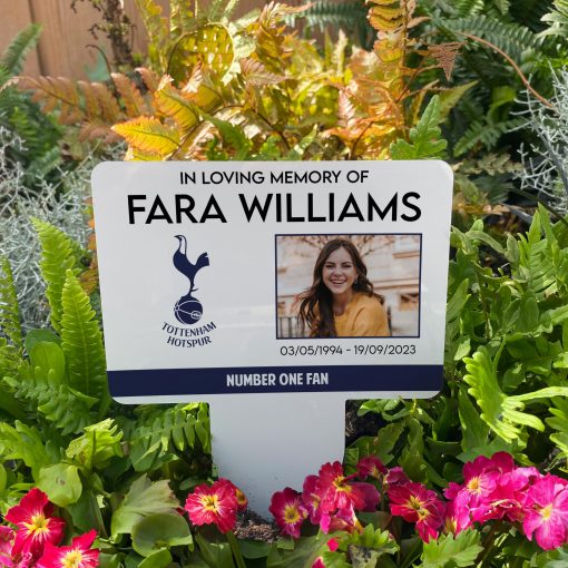 White Tottenham Hotspur football club memorial stake inserted in flower bed surrounded by colourful flowers in the garden