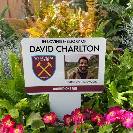White West Ham United football club memorial stake inserted in flower bed surrounded by colourful flowers in the garden